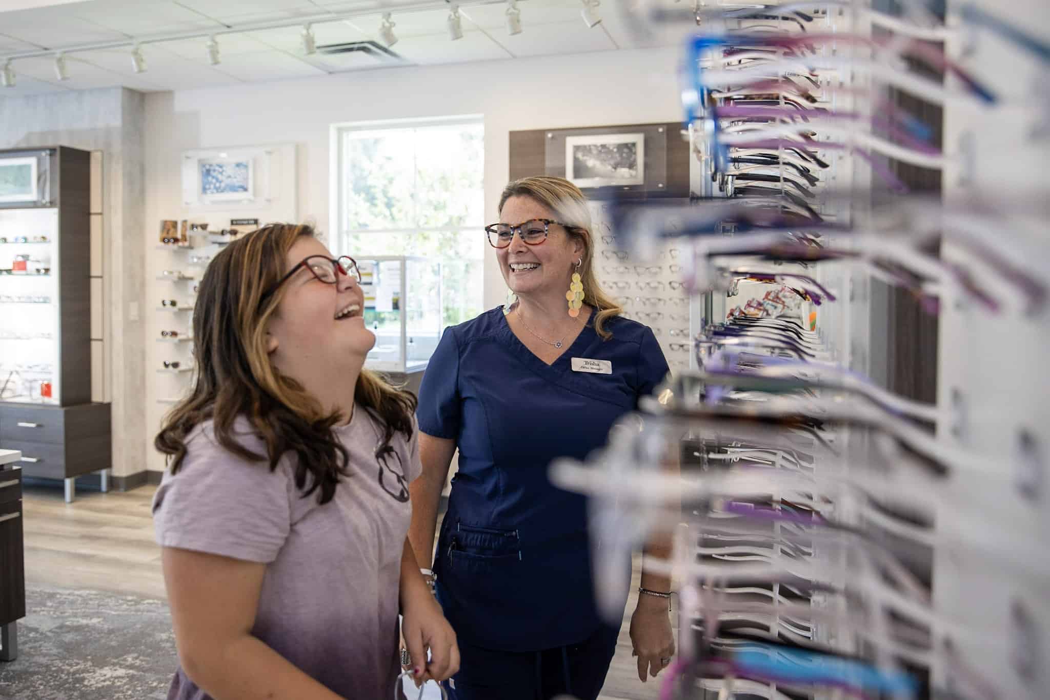 Family Eye Care Office Manager laughing with young female customer while browsing eyeglasses selection in the Bristol office.