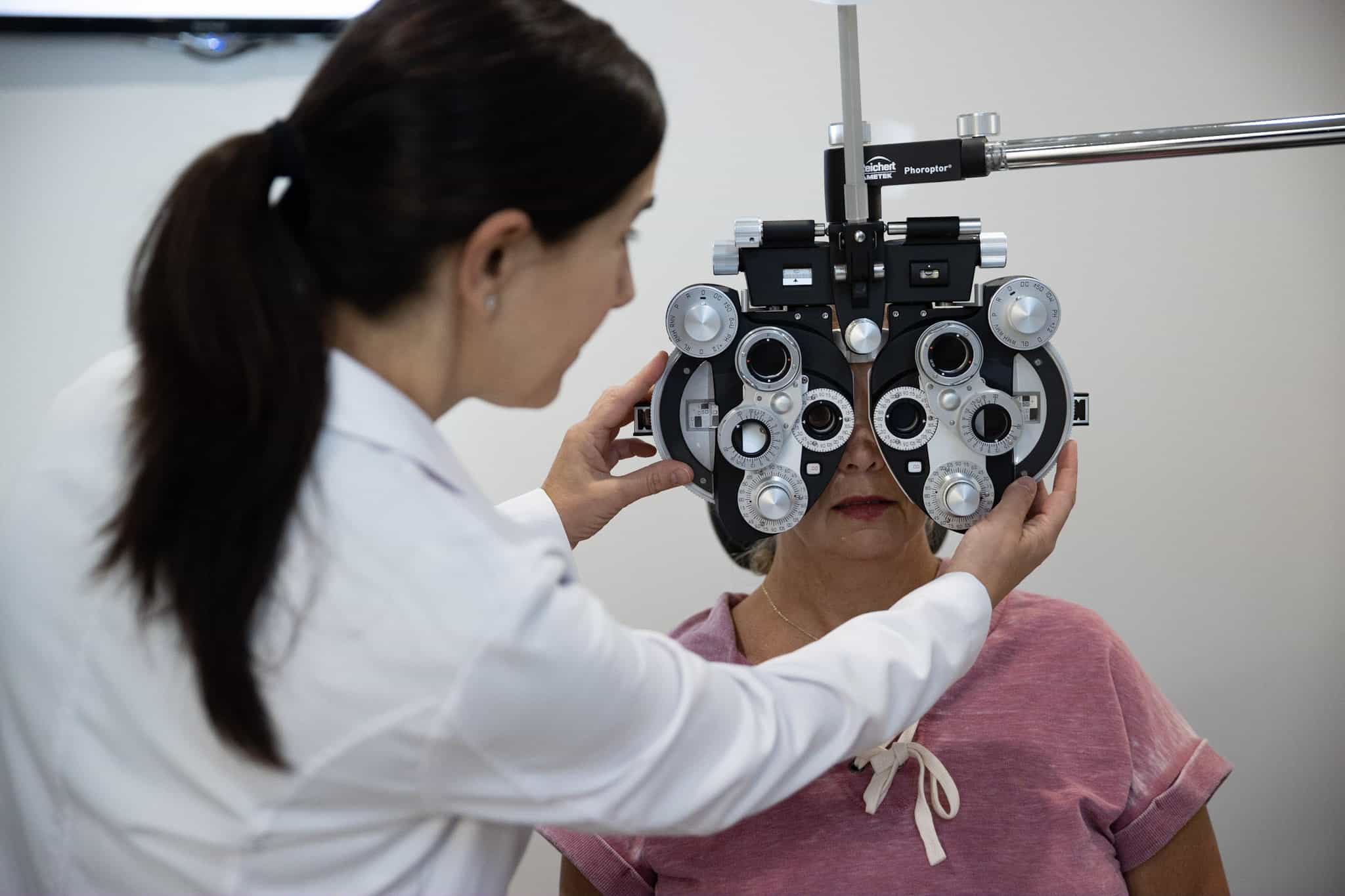 Dr. Helen J. Zervas of Family Eye Care positioning a phoropter up to a female patient to examine her vision.